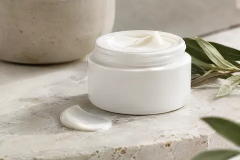 Flacon blanc compact de crème hydratante posé sur une pierre claire avec une touche de texture crémeuse