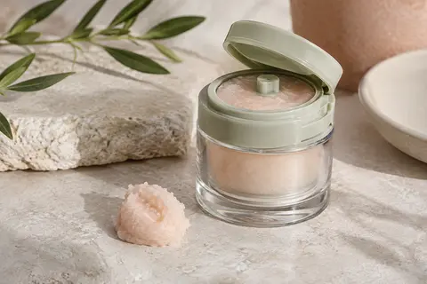 Baume démaquillant compact à texture sorbet posé sur une pierre claire, avec une petite noisette de produit.