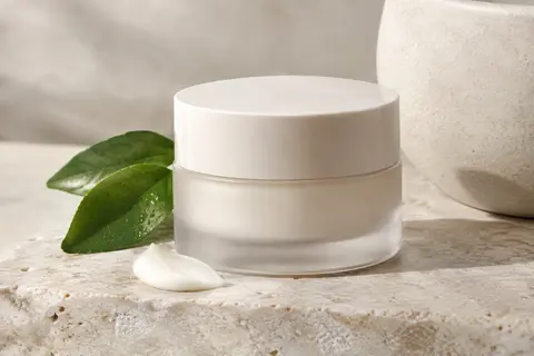 Sérum-crème visage posé sur une pierre claire, accompagné d’une touche de crème et d’un feuillage discret.
