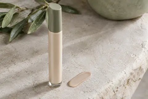 Fluide solaire visage SPF 50 posé sur une pierre claire, avec une trace de texture légère à proximité.