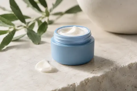 Petit contenant bleu de crème contour des yeux posé sur une pierre claire dans une lumière douce.