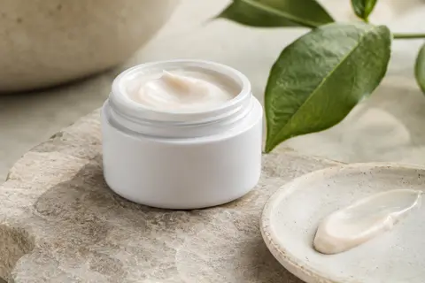 Crème contour des yeux blanche à la texture riche, posée sur une pierre claire dans une lumière douce.